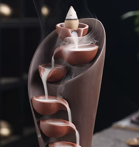 Ambiance de méditation avec porte-encens cascade et cône à reflux en cours de combustion.